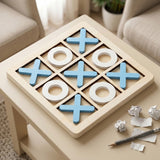 A wooden tic-tac-toe game board with blue X marks and white O rings, placed on a beige table in a living room setting with crumpled paper and a pencil nearby.