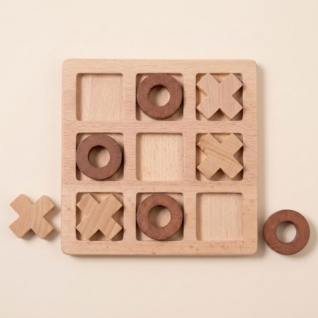 A wooden tic-tac-toe game board with a natural light wood finish, featuring carved squares and circular holes. Two dark brown wooden pieces are placed on the board, and two additional loose pieces sit nearby on a warm cream background.