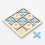 A wooden tic-tac-toe game board with a light natural wood frame, blue X pieces, and white O rings, shown on a clean white background with one loose blue X piece beside the board.