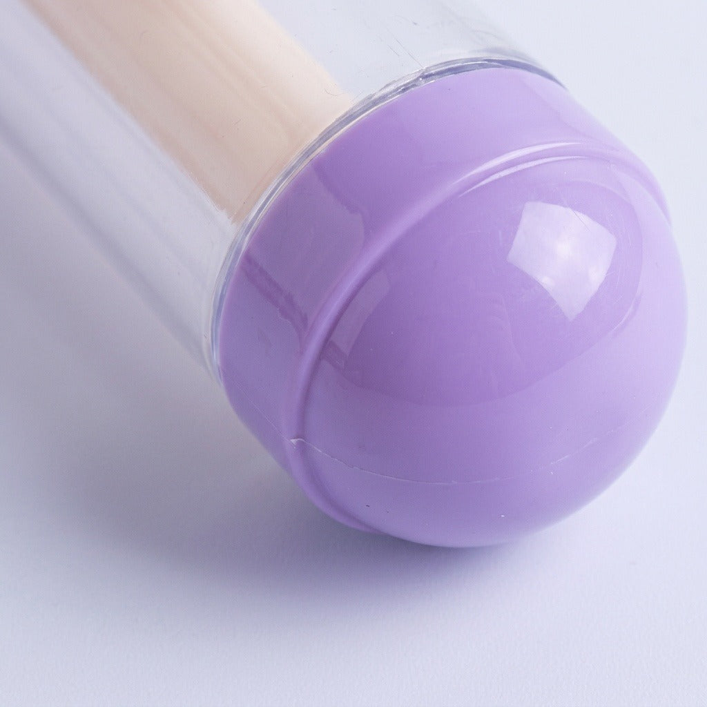 A close-up shows the water gun's rounded purple end cap, clear barrel edge, and cream inner shaft against a pale background.