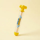 A plastic toy water gun with a clear barrel, yellow top and bottom caps, and blue and yellow 'mix and pour WATER' graphics on the side, shown on a light beige background.
