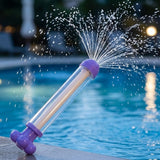 A purple water gun with a clear barrel sprays a wide fan of water beside a swimming pool at night.