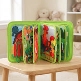 Green fabric busy book stands with farm animal activity pages fanned open on a light wooden table in a nursery.