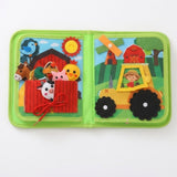 Green fabric busy book open flat on white, with animal puppets tucked into a red barn pocket beside a yellow tractor.