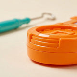 Buzz wire game close-up shows an orange plastic base on a cream surface, with a blurred turquoise loop wand behind it.
