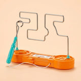 Orange plastic buzz wire game has a silver wire course, turquoise loop wand, and white cord against a peach background.