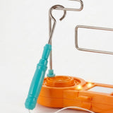 Buzz wire game close-up shows a turquoise wand loop around the silver wire course above an illuminated orange plastic base against white.
