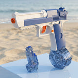 Blue-and-white plastic water gun sprays water beside a smaller transparent reservoir on a white platform at a sandy beach.