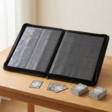 Open black trading-card binder with empty clear pockets rests upright on a wooden desk beside loose cards and two card stacks.