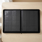 Open black trading-card binder lies flat on a pale wooden desk, showing two empty pocket pages and a perimeter zipper.