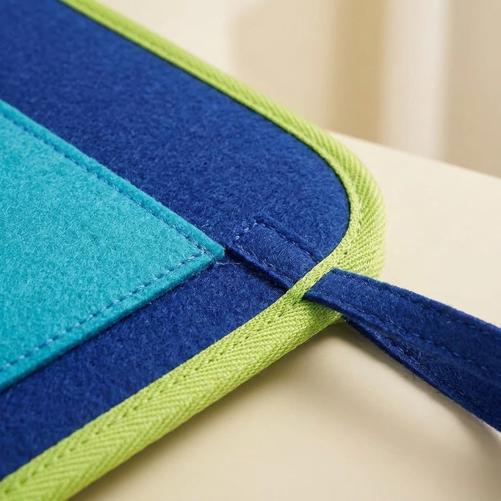 Close-up of a blue felt busy board showing lime green edging, a turquoise stitched patch and a blue carrying loop.