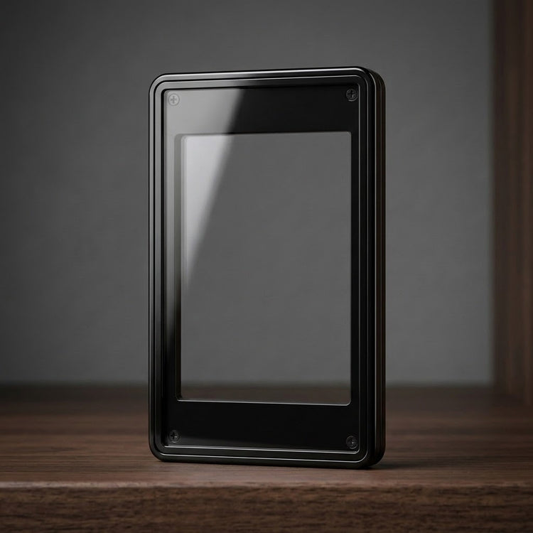 Black graded card protector with a clear central window and four visible corner screws stands upright on wood against a gray background.