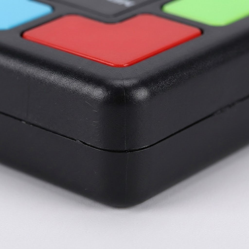 An electronic memory game close-up shows its rounded black plastic casing, red button, and partial blue and green buttons against white.
