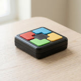 A black plastic electronic memory game with four colored buttons rests on a light wooden tabletop beside a window.