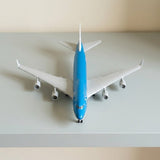 Blue and white diecast alloy aircraft model seen from above on a light grey shelf, showing swept wings and four engines.