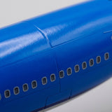 Close-up of a diecast aircraft model's glossy blue fuselage with rows of passenger windows against a pale background.