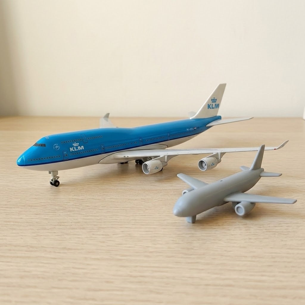 A blue and white aircraft model stands beside a smaller gray aircraft model on a light wooden tabletop against a beige wall.
