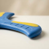 Close-up of a blue EVA foam boomerang arm showing yellow detailing, shallow grooves and a rounded edge on a cream surface.