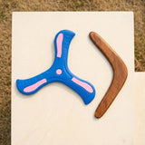 A blue and pink plastic throwing disc and a wooden boomerang lying on a white stone slab outdoors.
