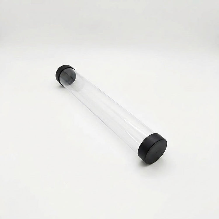 Empty transparent playmat storage tube with black end caps lies diagonally on a white background.