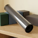 Clear playmat storage tube with dark ends rests diagonally against coloured storage boxes on a wooden shelf.