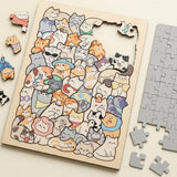 A wooden jigsaw puzzle featuring a dense collage of cute, hand-drawn cartoon cats in many colors, shown on a light beige surface with several loose pieces around it and a stack of gray puzzle pieces on the right.