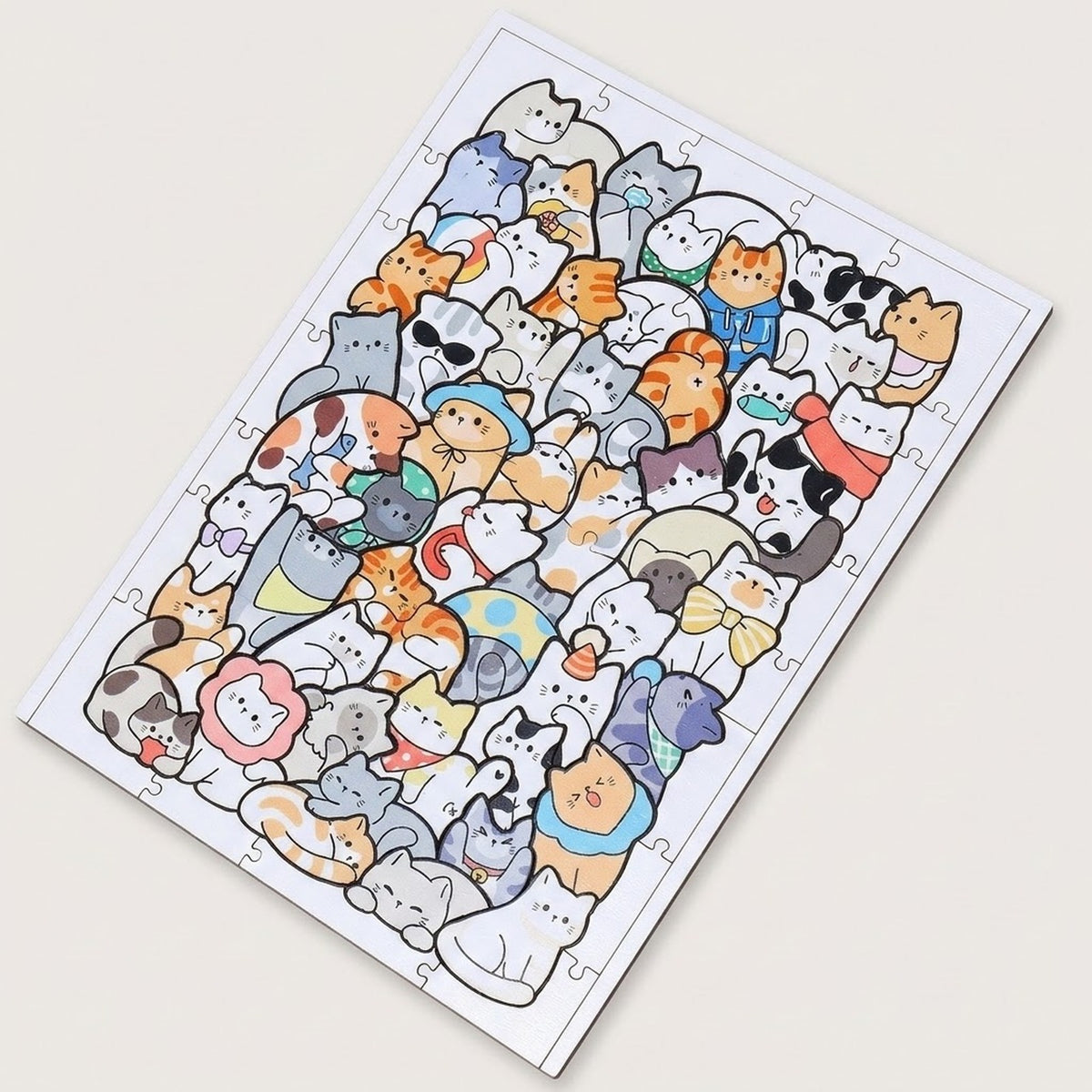 A completed jigsaw puzzle featuring a dense collage of cute cartoon cats in many colors, photographed at an angle on a plain light beige background.