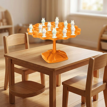 Orange plastic balancing game with white rabbit pieces stands on a wooden children's table surrounded by chairs in a sunlit room.
