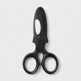 Black safety scissors with a white orca marking and round finger loops lie closed on a light gray background.