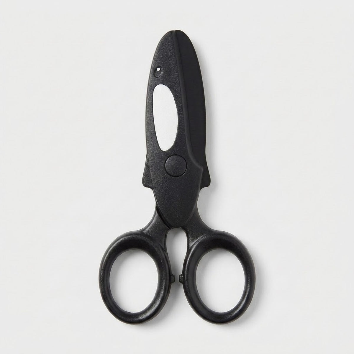 Black safety scissors with a white orca marking and round finger loops lie closed on a light gray background.