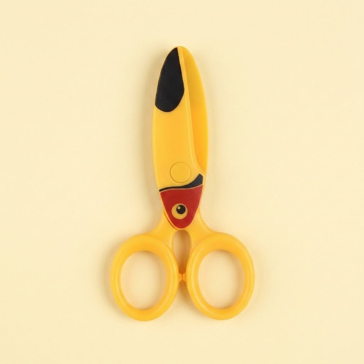 Yellow safety scissors with a red bird face and black beak detail lie closed on a pale yellow background.