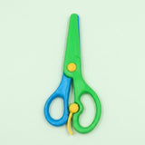 Green and blue safety scissors with yellow pivot and lever details lie closed on a pale green background.