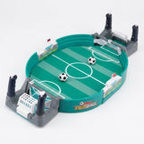 A tabletop soccer game set with a green turf-style field, gray goals, black-and-white soccer balls, and small player figures, photographed on a clean white background.