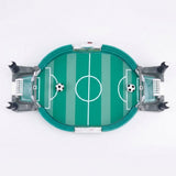 Green tabletop soccer game viewed from above with white field markings, gray goals, and two balls against a white background.