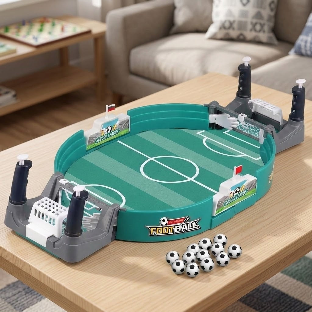 A tabletop soccer/football game set displayed on a light wood table in a living room setting. The product includes a green soccer field oval, gray and white goal structures with black handles, small black-and-white soccer balls, and a visible 'FOOTBALL' logo on the front.