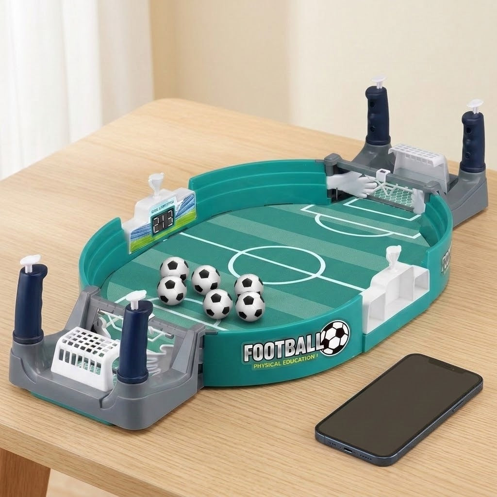 A tabletop view of a green and teal soccer-themed physical game board with small soccer balls, goal posts, and a smartphone placed beside it on a light wood table.