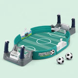 A children's tabletop football game with a green turf-style field, gray goal areas, white goals, and two black-and-white soccer balls on a pale mint background.
