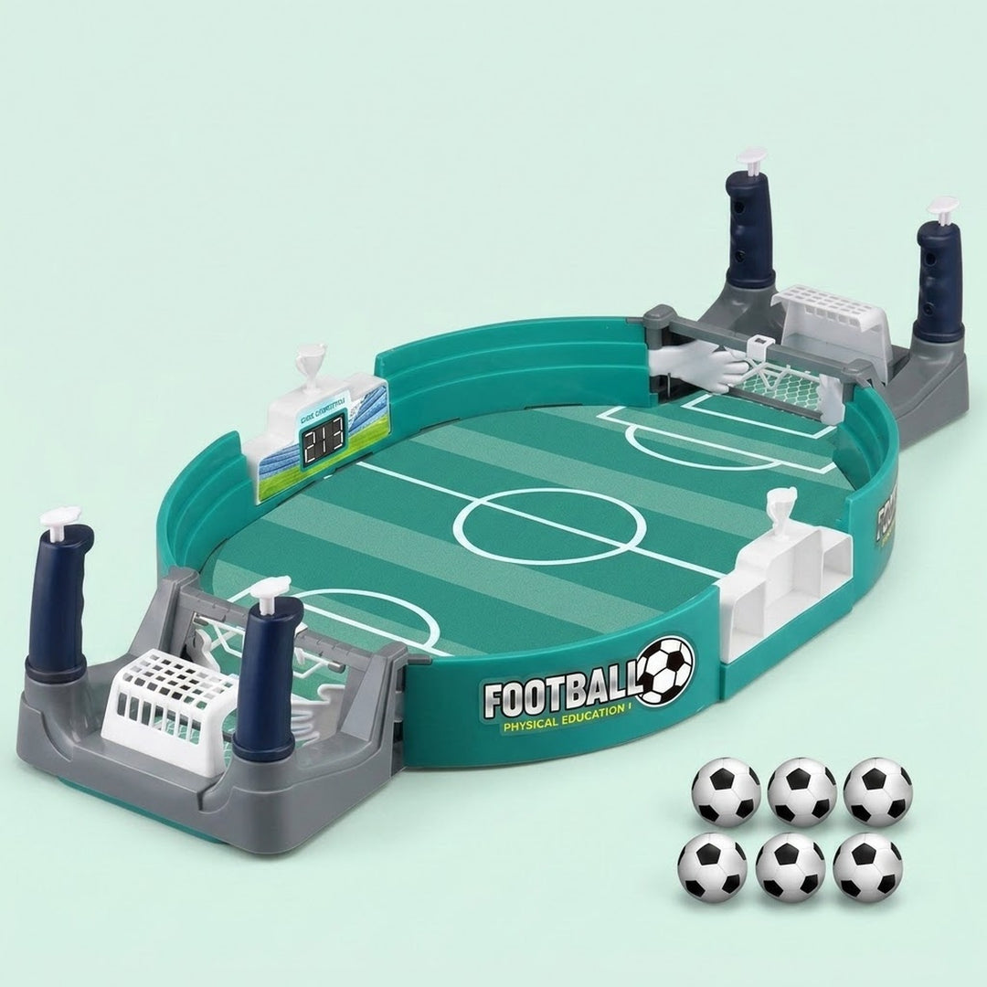 A children's tabletop soccer game set on a pale mint background. The oval green field toy has white soccer markings, gray goal frames, dark blue posts, and six black-and-white soccer balls placed in front.