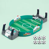 A tabletop soccer game set with a green field court, gray goals and posts, white net areas, and several black-and-white soccer balls on a pale mint background.