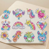 Diamond painting kit with twelve multicoloured gem stickers arranged on a cream notebook resting on a pale wooden surface.