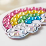 Diamond painting kit rainbow sticker close-up showing raised pink, yellow, green, blue and clear faceted gems on a white surface.
