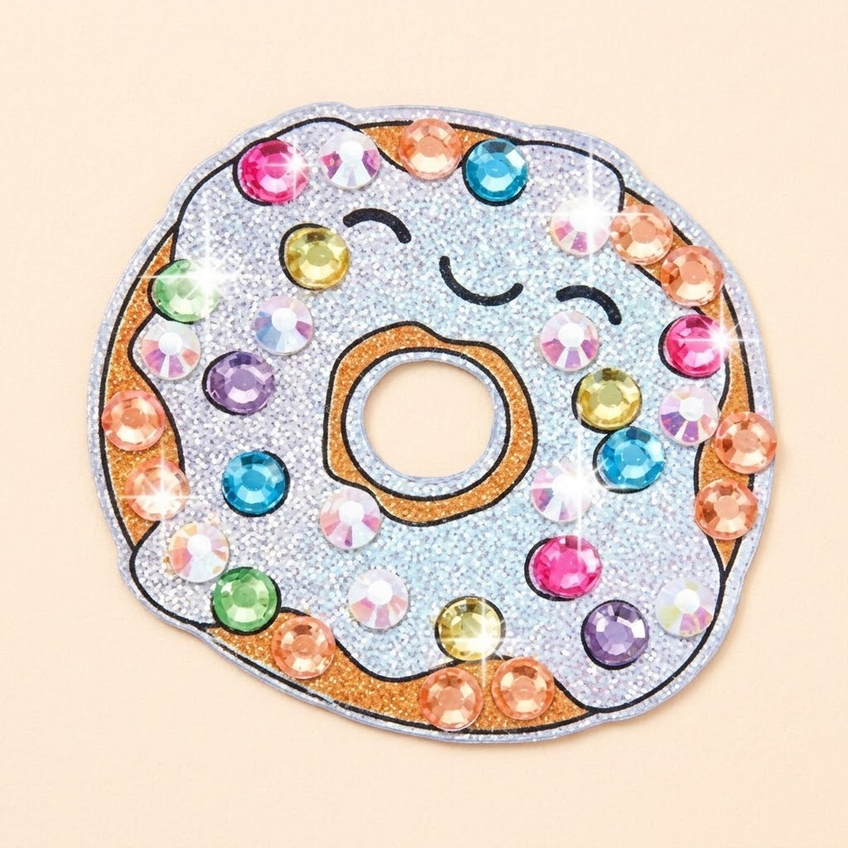 Diamond painting kit donut sticker with silver glitter icing, colorful faceted gems, and a smiling face on a pale peach background.
