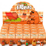 A retail display box filled with small Capybara-themed keychain packs, with several Capybara keychains displayed in front. The packaging features a warm orange and beige gingham pattern with cartoon capybaras and Chinese text.