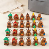 A set of small bear-shaped keychains arranged in rows on a light surface, with a cream tote bag and a gray pouch in the background. The keychains feature various cute character designs and accessories in brown, green, red, yellow, orange, and blue.