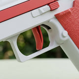 Close-up of a water gun showing its red trigger, white trigger guard, and textured red grip against blurred greenery.