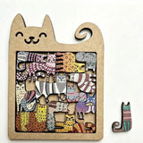 A wooden jigsaw puzzle with colourful cat pieces sits in a natural brown cat-shaped frame beside one loose piece on a white background.