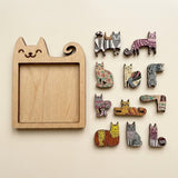 An empty wooden cat-shaped jigsaw puzzle frame lies beside neatly arranged colourful cat pieces on a cream background.