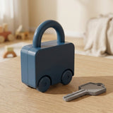 A dark blue vehicle-shaped lock puzzle stands closed beside a gray key on a wooden table in a softly blurred room.