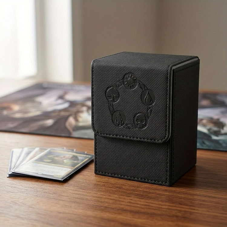 Closed black textured PU leather deck box with embossed symbols stands beside sleeved cards on a wooden table near a window.