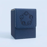 Blue textured card deck box with gray lining, stitched edges, and dark embossed symbols on its front flap against a pale blue background.